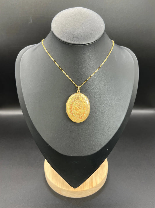 An oval floral engraved locket, with a chain, on a black bust