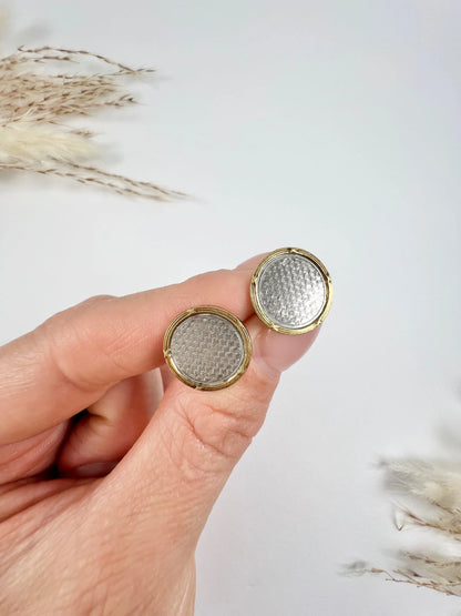 A pair of circular platinum and yellow gold cufflinks, held in a hand