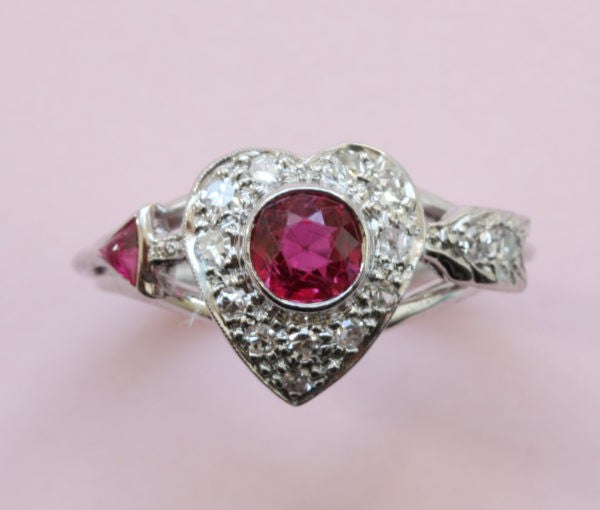 Vintage 1950s Ruby and Diamond Heart and Arrow Ring; 0.75ct round old-cut ruby surrounded by 0.30cts diamonds, in platinum and white gold
