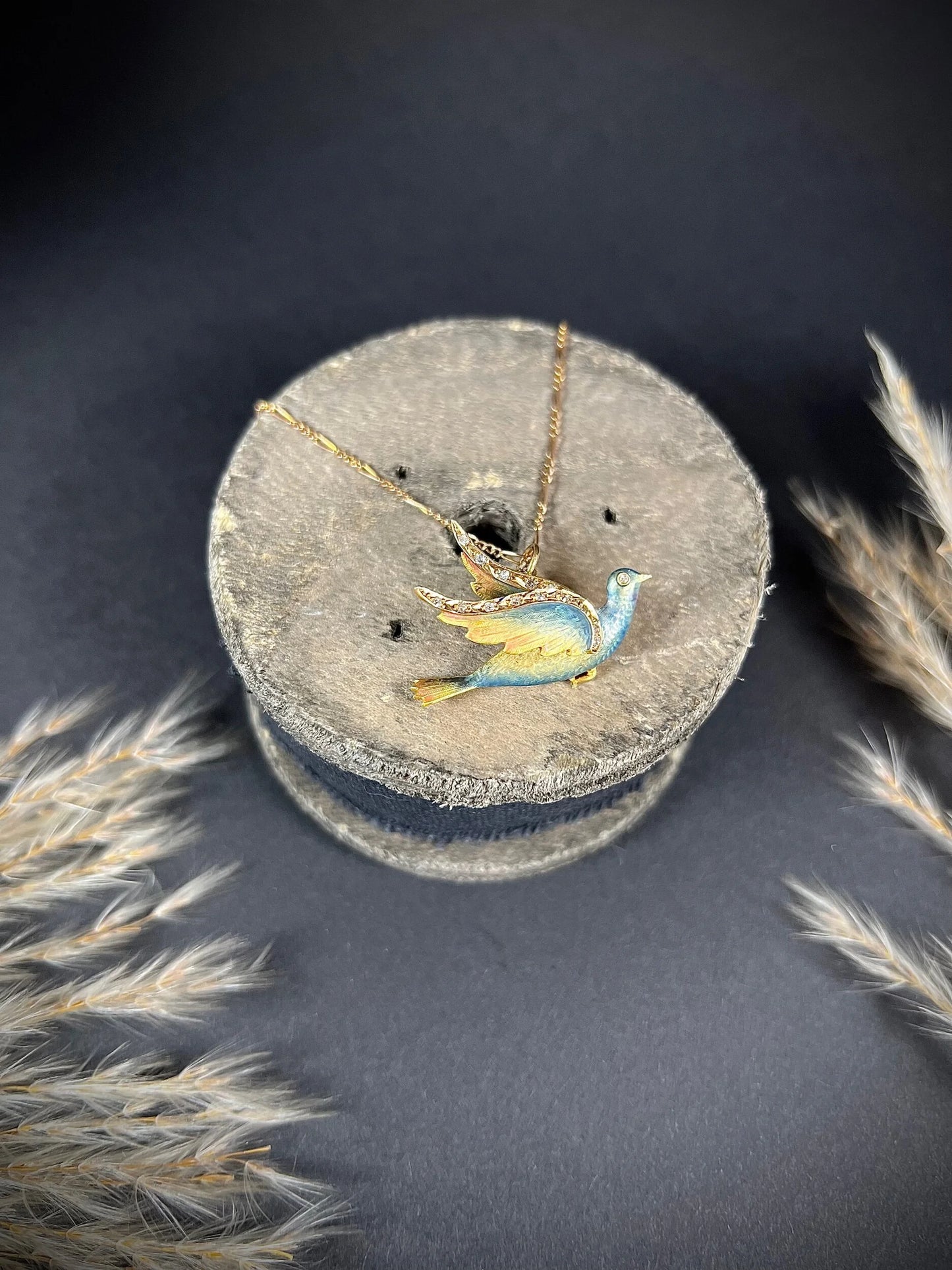 An enamel and diamond dove bird pendant, with a chain, on a wooden spool
