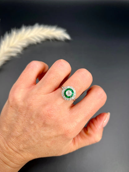 An emerald and diamond target cluster ring in platinum, modelled on a hand
