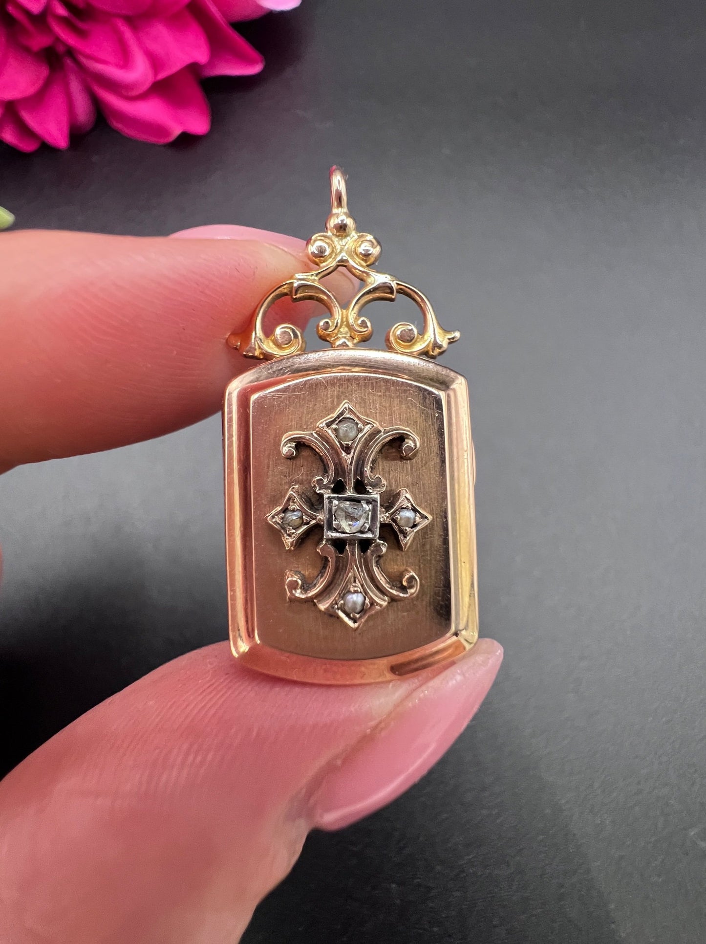 A yellow gold ornate locket with diamond fleur-de-lis detail, held in a hand