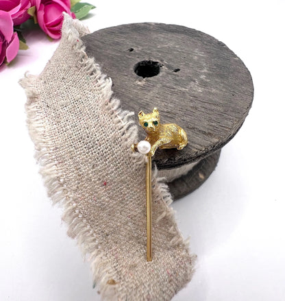 A yellow gold cat playing with a pearl ball stick pin