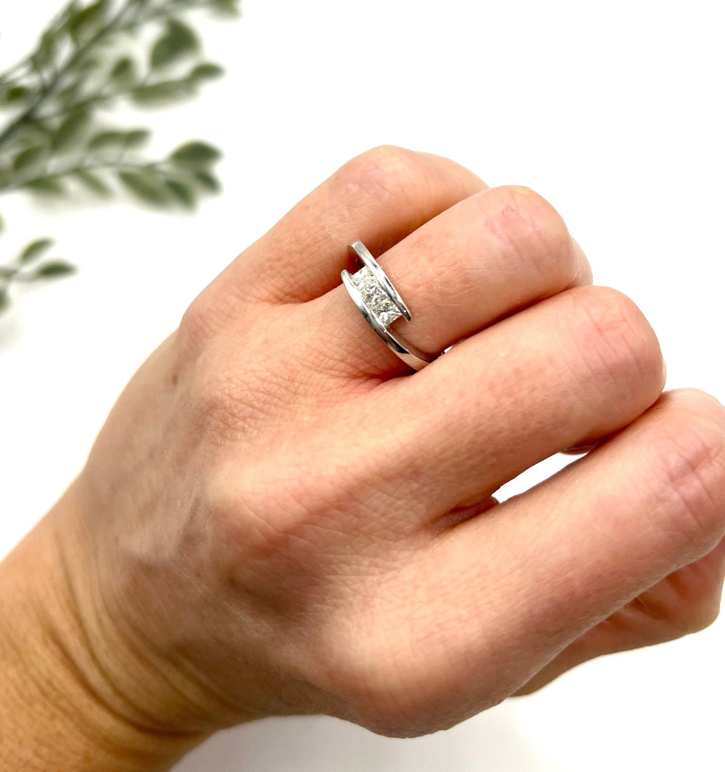 A three stone princess cut diamond crossover ring in white gold, modelled on a hand