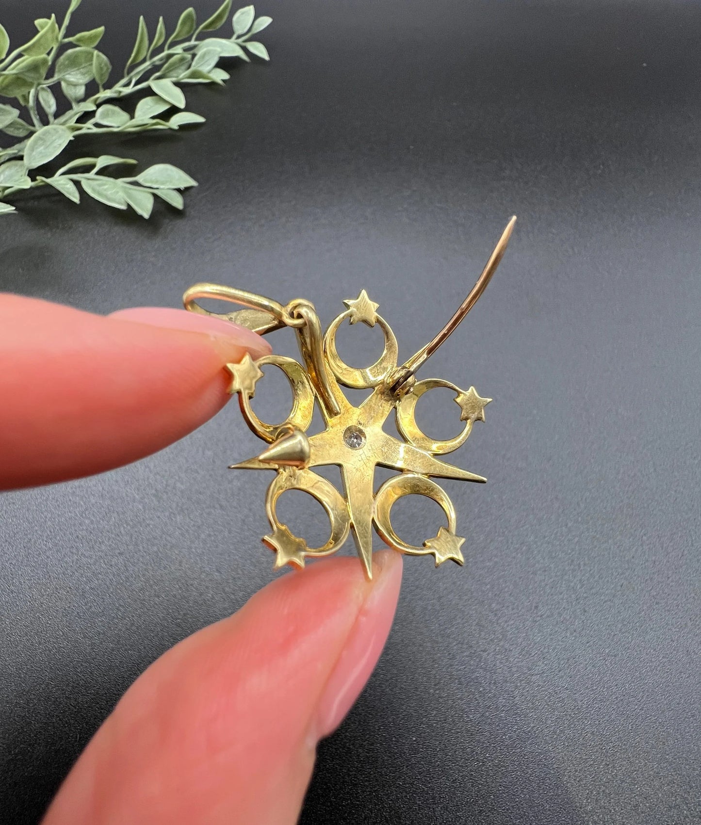 A yellow gold star and crescent brooch/pendant set with a diamond and pearls, held in a hand