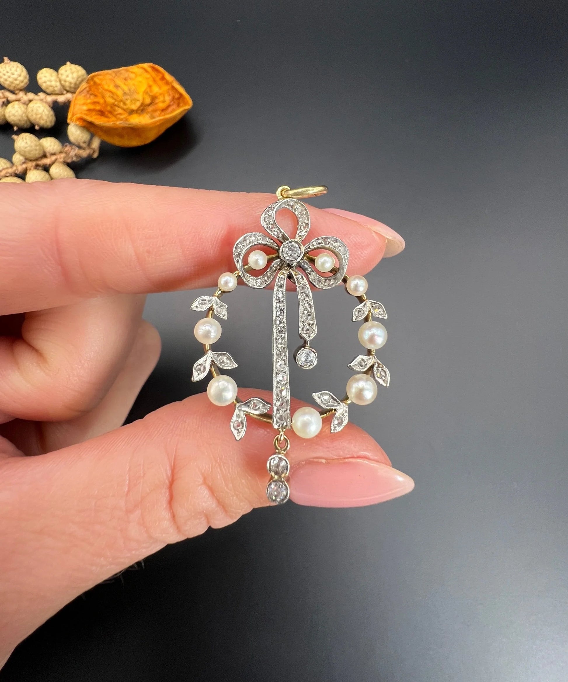 A pearl and diamond bow pendant in gold and platinum, held in a hand