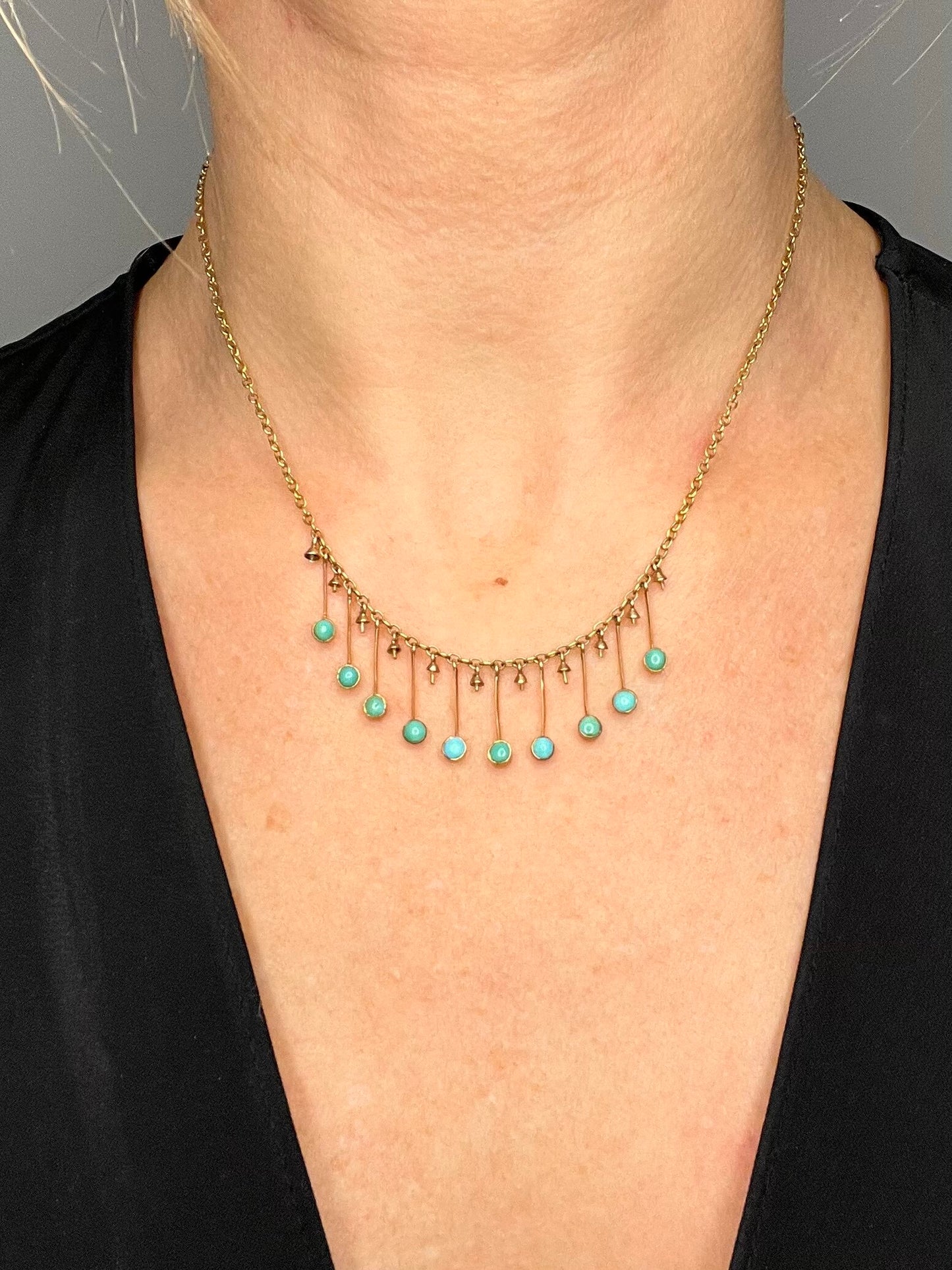 A gold negligee pendant necklace with turquoise drops, modelled by a woman