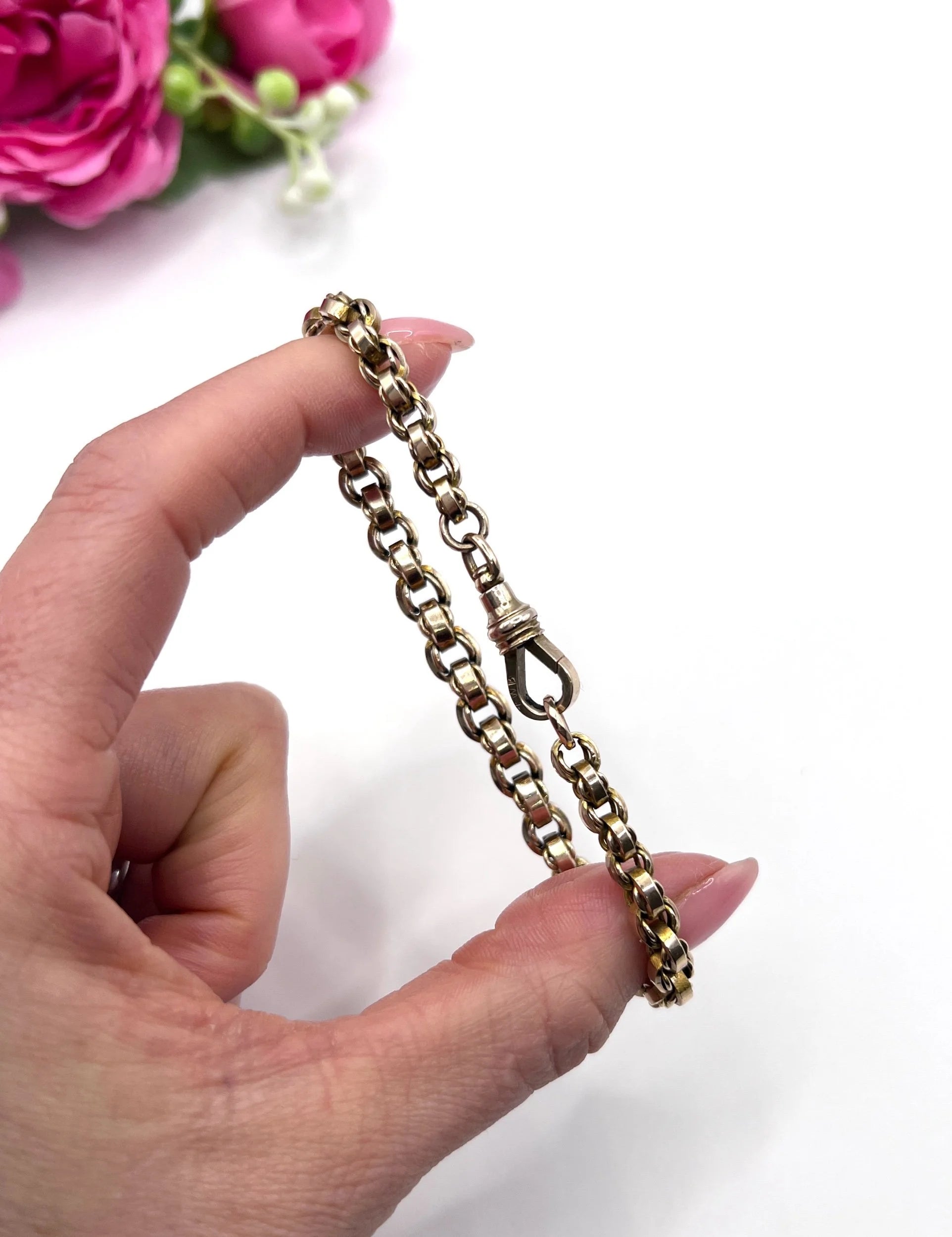 A gold round link bracelet with a lobster claw clasp, held in a hand