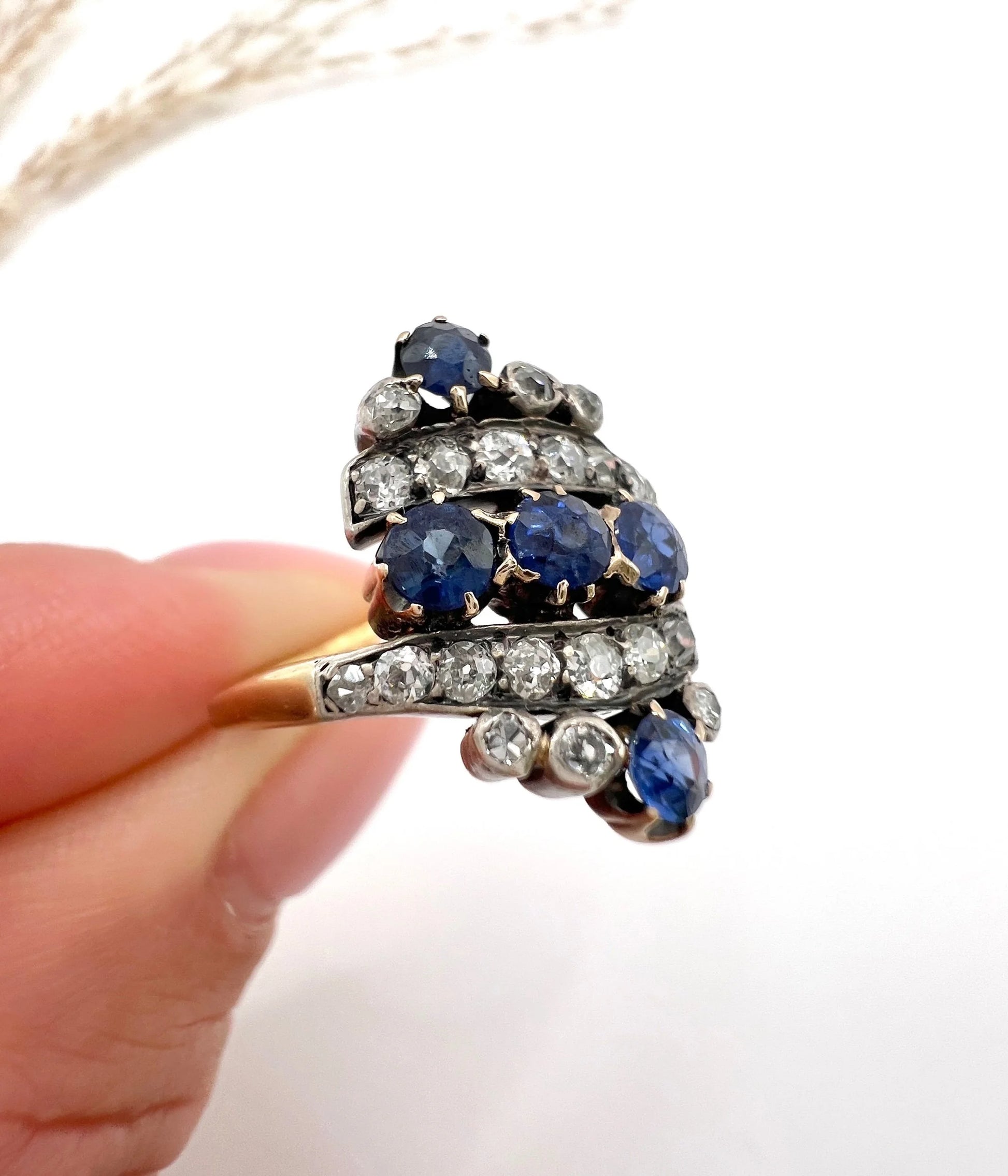 A navette shaped sapphire and diamond ring in yellow gold, held by a hand