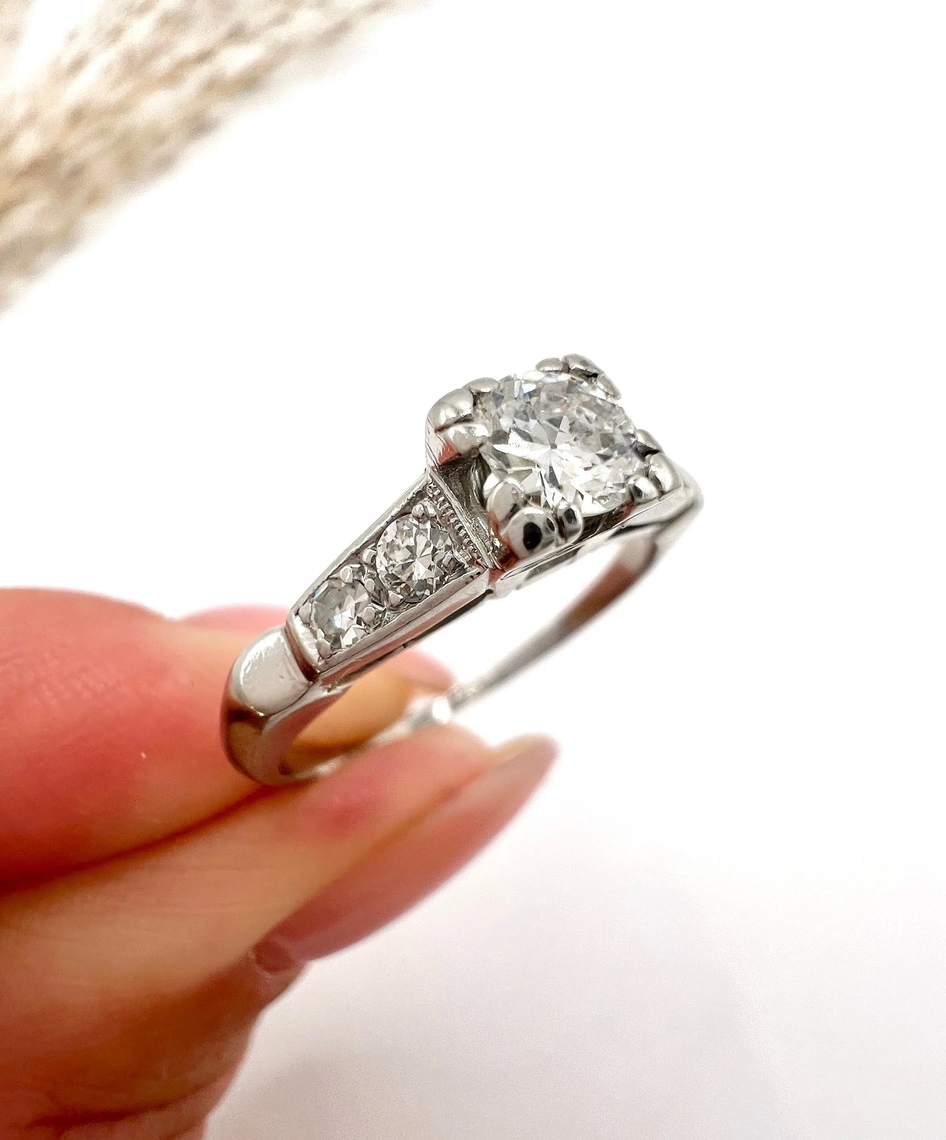 A solitaire diamond ring in platinum, with diamond set shoulders, held in a hand