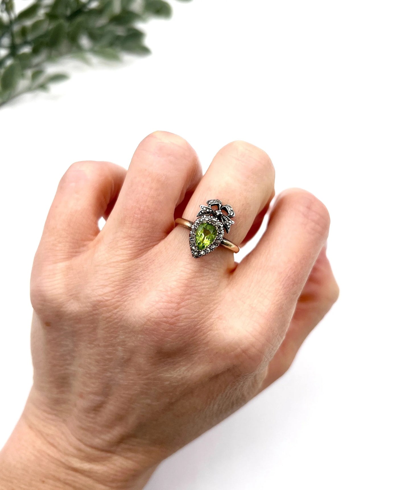 A pear cut peridot and round diamond cluster ring with bow detail, in yellow gold and white metal, modelled on a hand