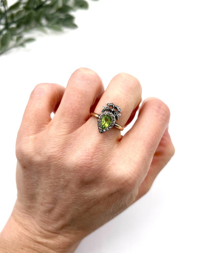 A pear cut peridot and round diamond cluster ring with bow detail, in yellow gold and white metal, modelled on a hand