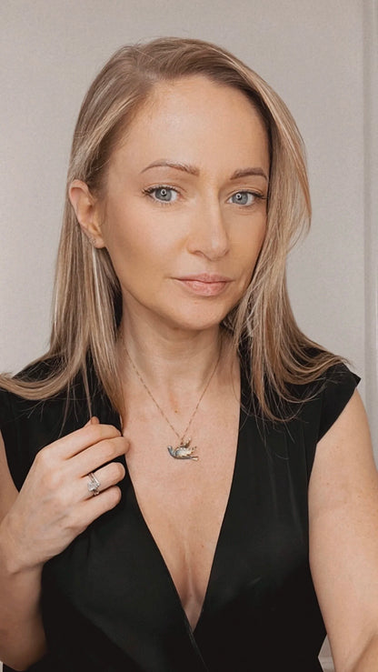 An enamel and diamond dove bird pendant, with a chain, modelled by a woman wearing a black top