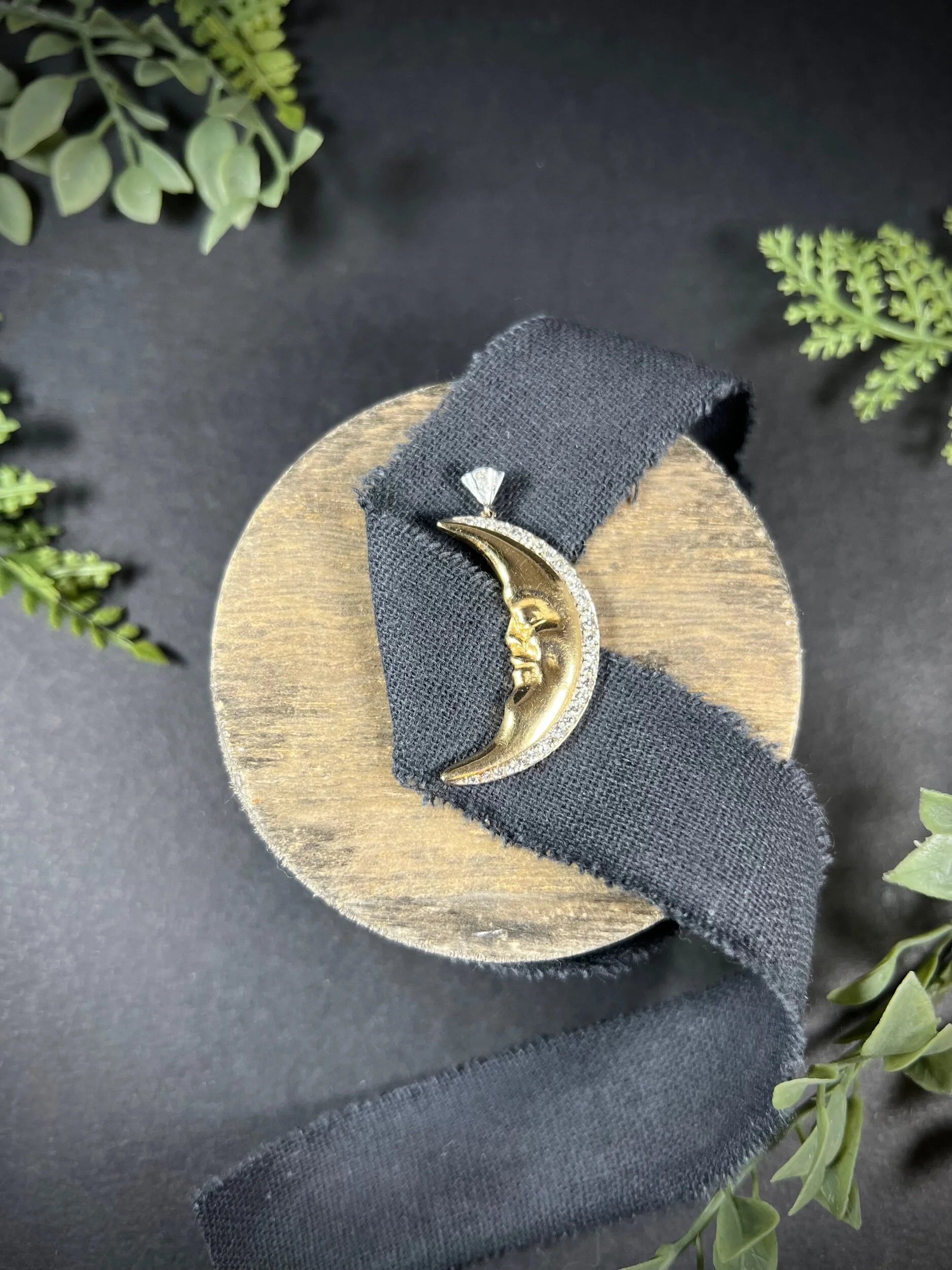 A gold crescent moon pendant with diamonds, on a black ribbon