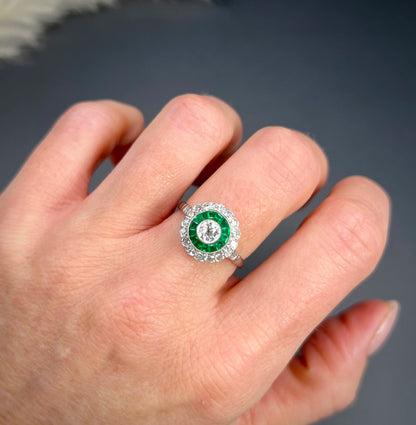 An emerald and diamond target cluster ring in platinum, modelled on a hand