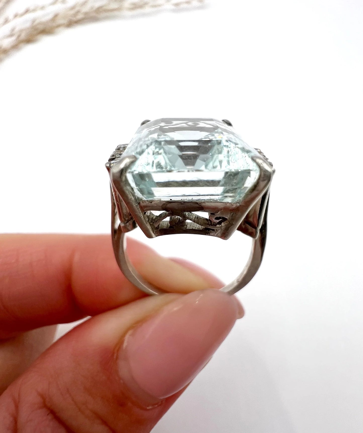 An aquamarine and diamond cocktail ring in white gold, held by a hand