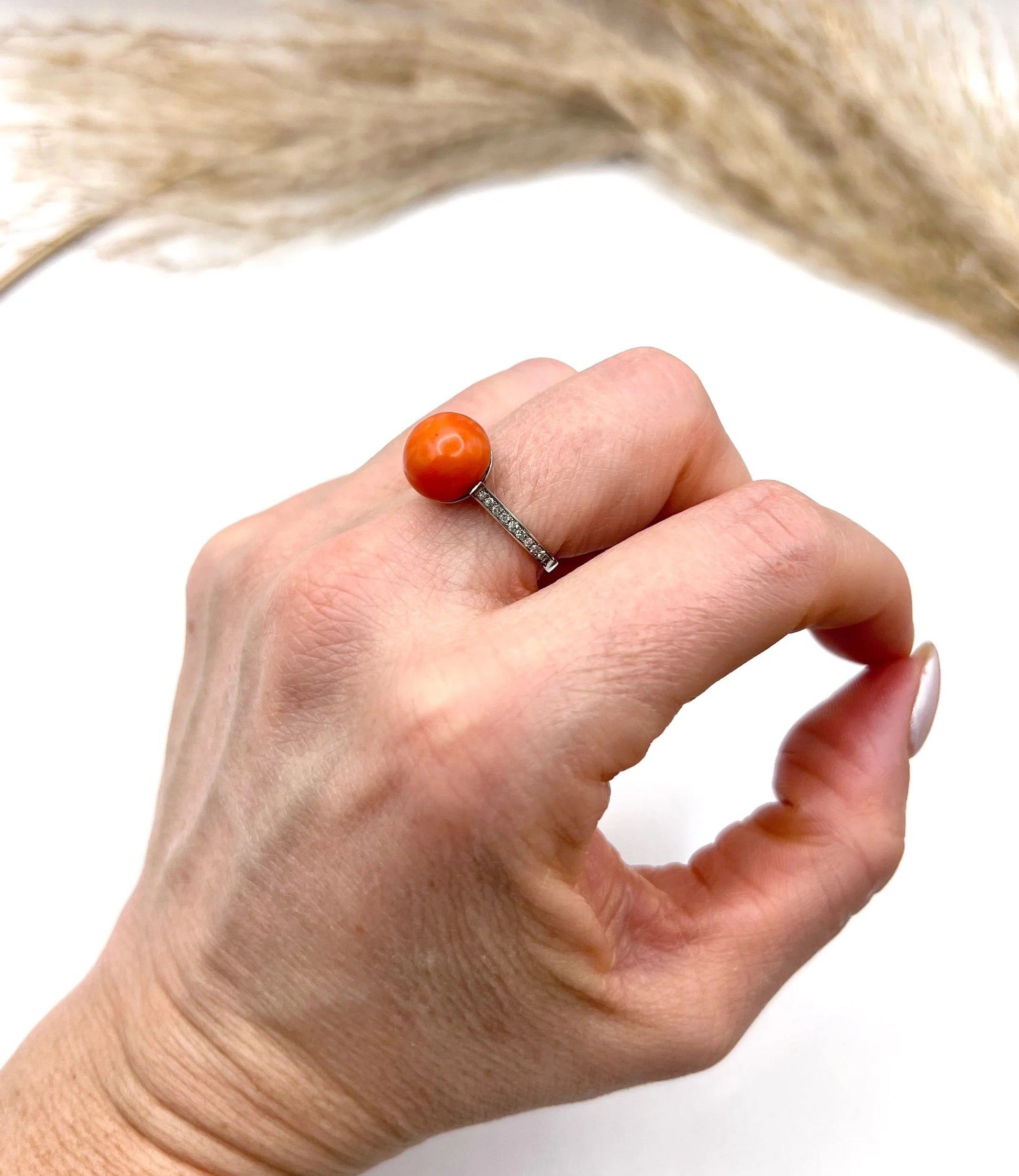A round orange coral and diamond dress ring in platinum, modelled on a hand