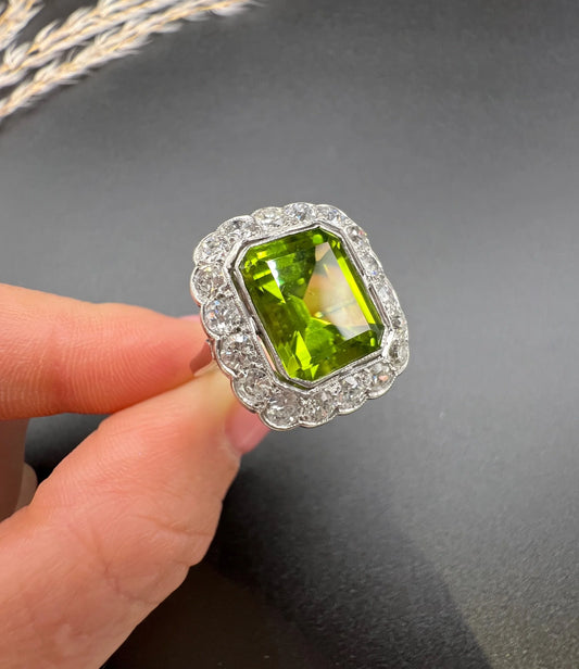 A cushion shaped peridot and diamond cluster ring in white metal, held in a hand