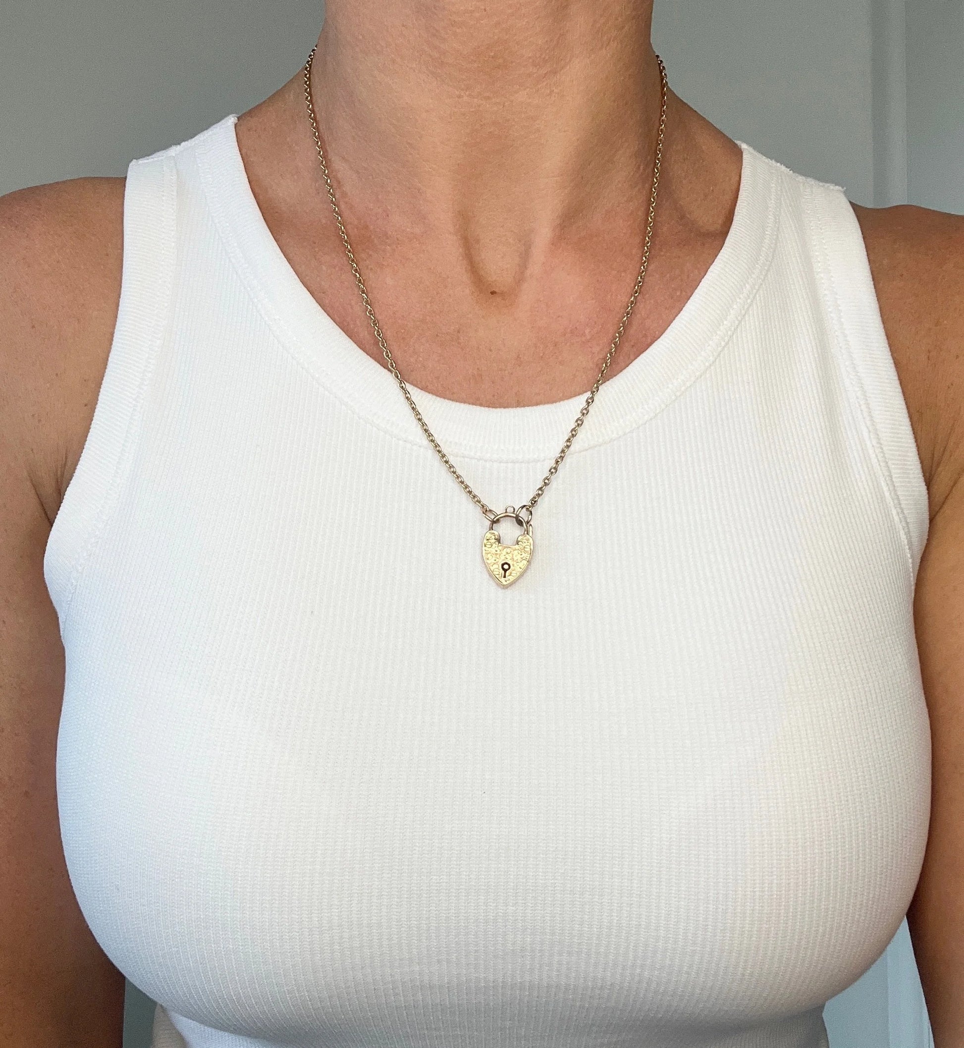 A gold chain necklace with gold heart padlock, modelled by a woman wearing a white top