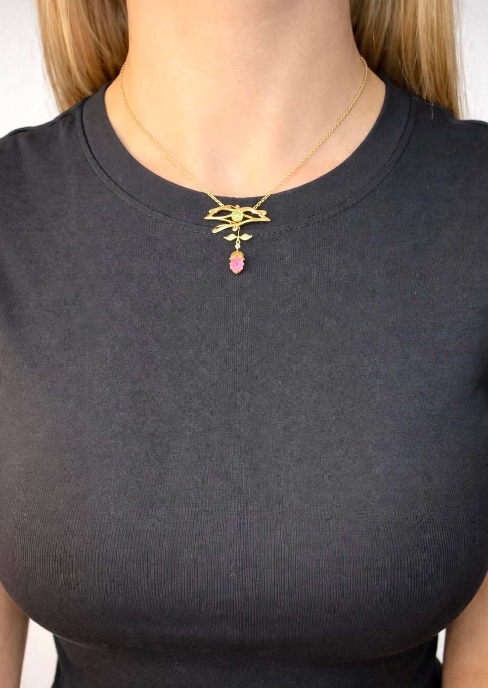 A yellow gold pendant necklace with pearls, a peridot, a diamond and a pink tourmaline drop, modelled by a woman wearing a black top
