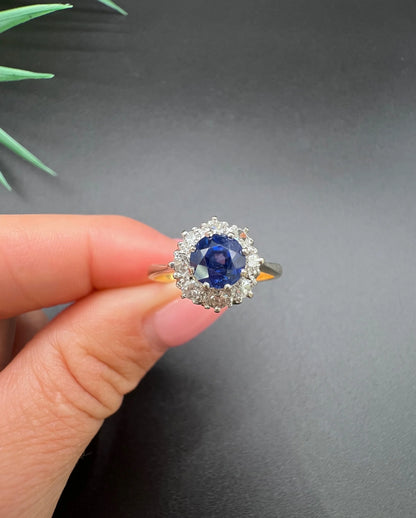 A circular cluster ring with sapphire and diamonds in yellow gold and platinum, held in a hand