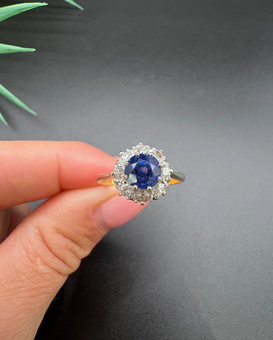 A circular cluster ring with sapphire and diamonds in yellow gold and platinum, held in a hand