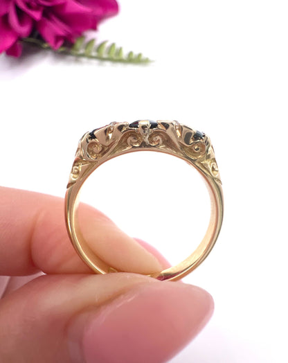 A seven stone sapphire and diamond carved ring in yellow gold, held in a hand