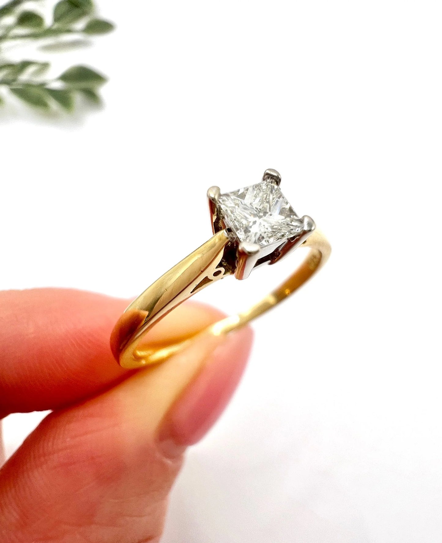 A solitaire princess cut diamond ring in yellow and white gold, held in a hand
