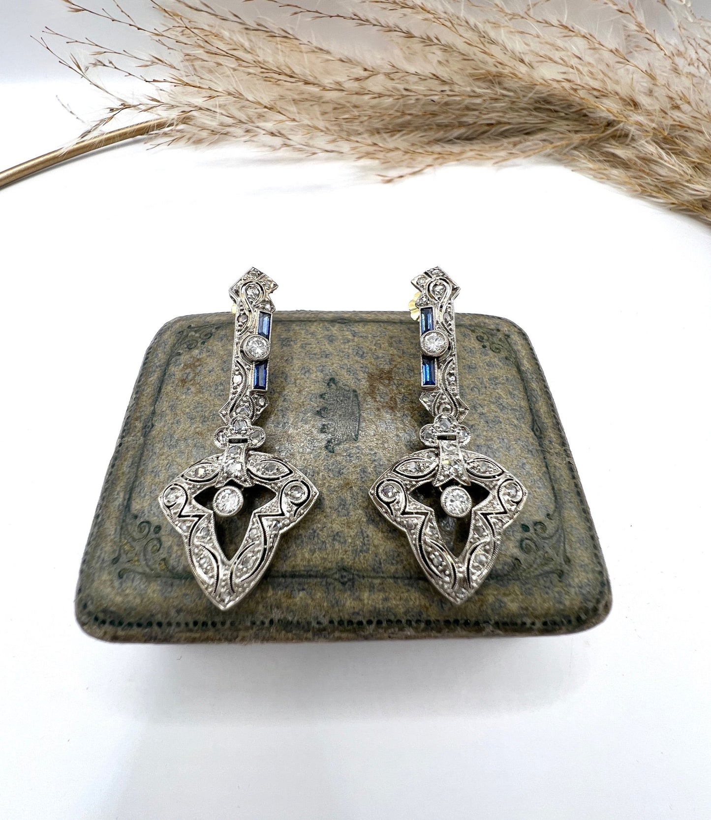 A pair of diamond and sapphire drop earrings, on an antique box
