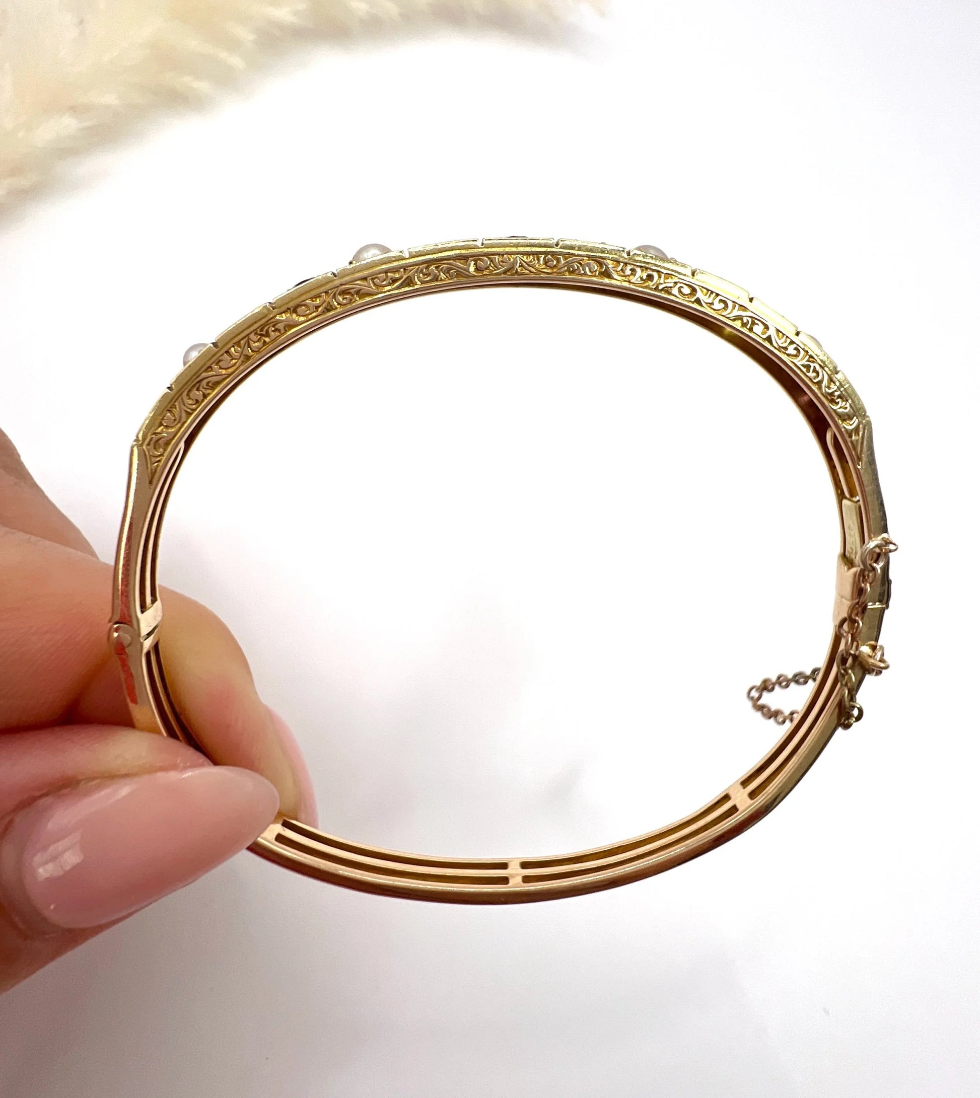 A yellow gold peridot, amethyst and pearl bangle bracelet, held in a hand
