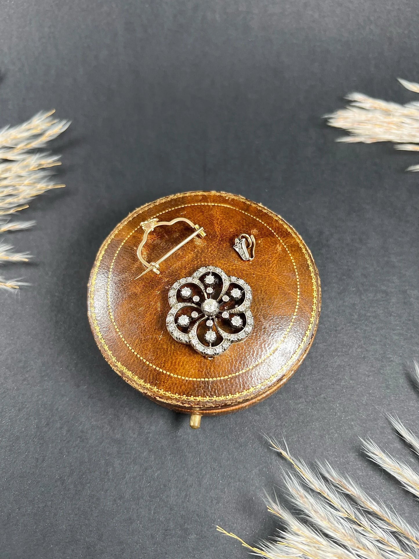 A floral design diamond set pendant/brooch on an antique brown jewellery box