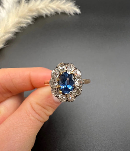 An antique sapphire and diamond oval cluster ring in yellow gold, held in a hand