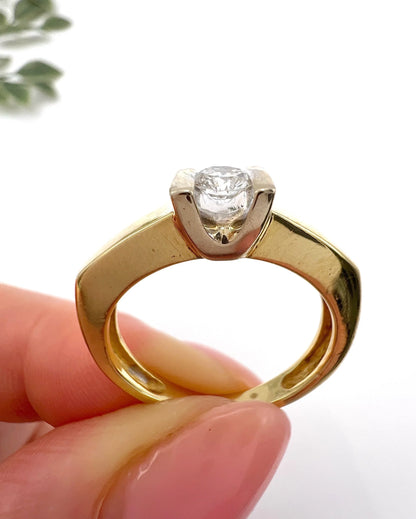 A brilliant cut diamond solitaire ring in yellow gold, held in a hand