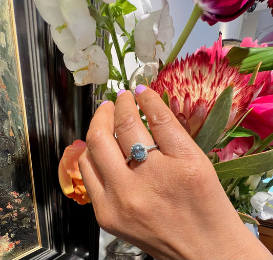 An oval aquamarine and round diamond cluster ring in white gold, modelled on a hand