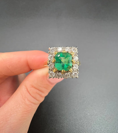 A square shaped emerald and diamond cluster ring in yellow and white gold, held in a hand