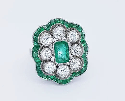 Vintage Emerald and Diamond Floral Cluster Dress Ring; emerald-cut emerald surrounded by eight round-cut diamonds and calibre-cut emeralds, in platinum