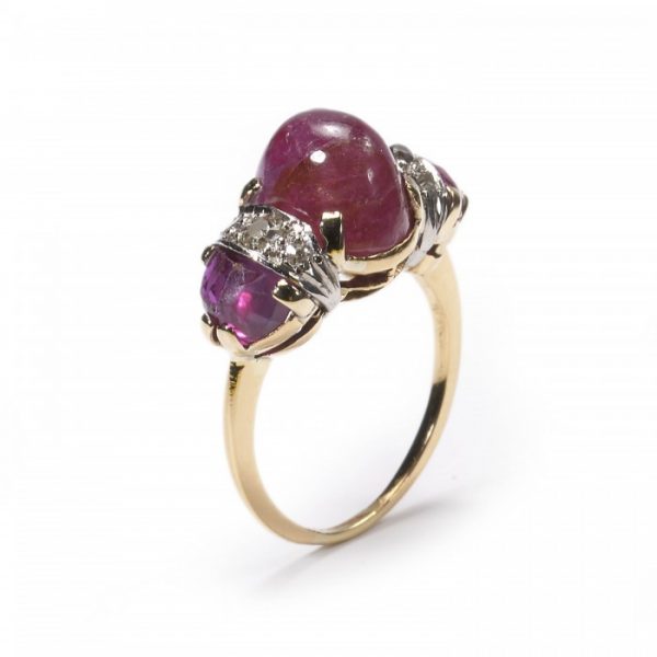 Vintage Cabochon Ruby and Diamond Three Stone Ring; central 4.80 carat cabochon-cut ruby, flanked by fancy faceted rubies and brilliant-cut diamonds, claw set in yellow gold. Circa 1950