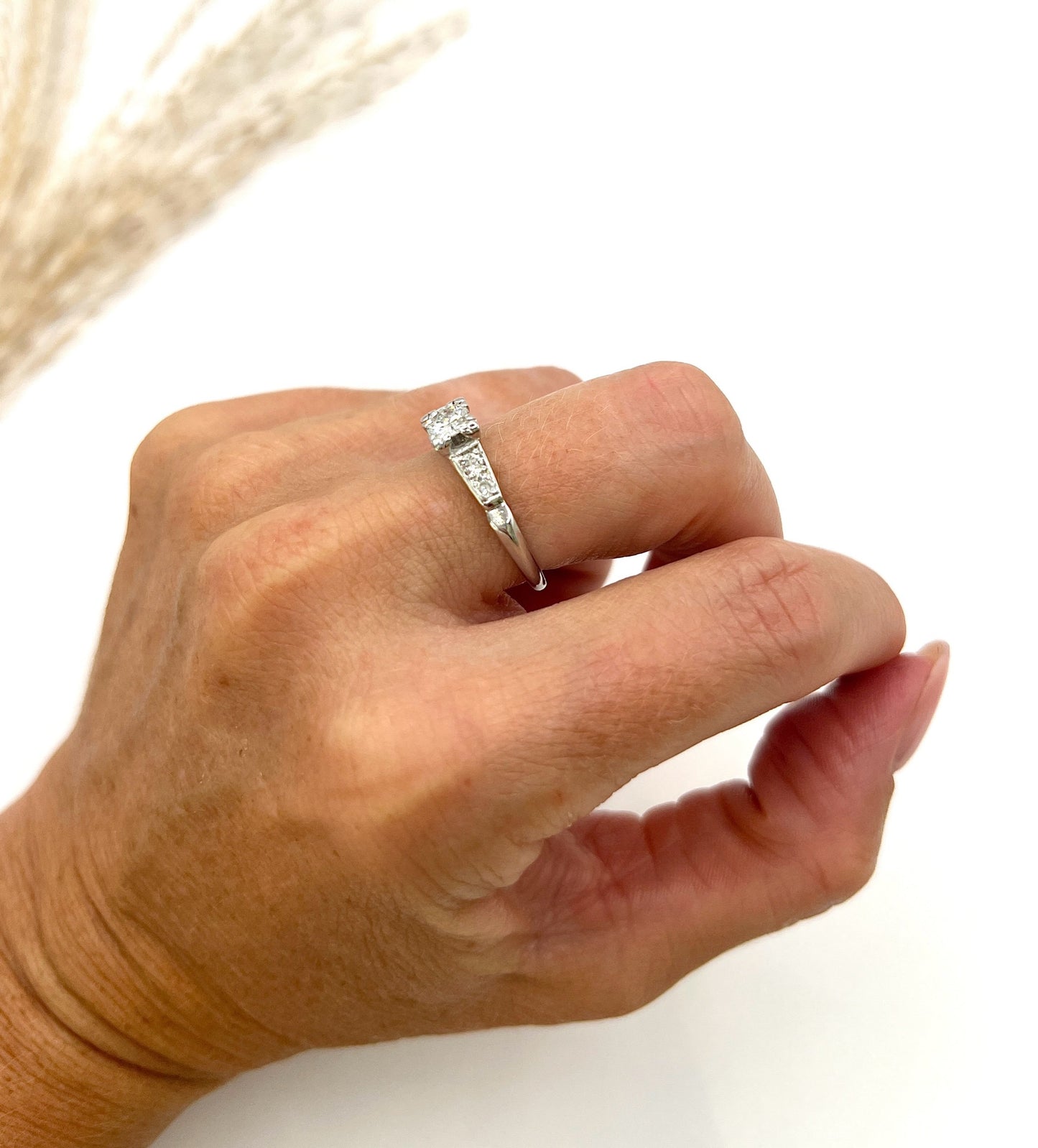 A solitaire diamond ring in platinum, with diamond set shoulders, modelled on a hand