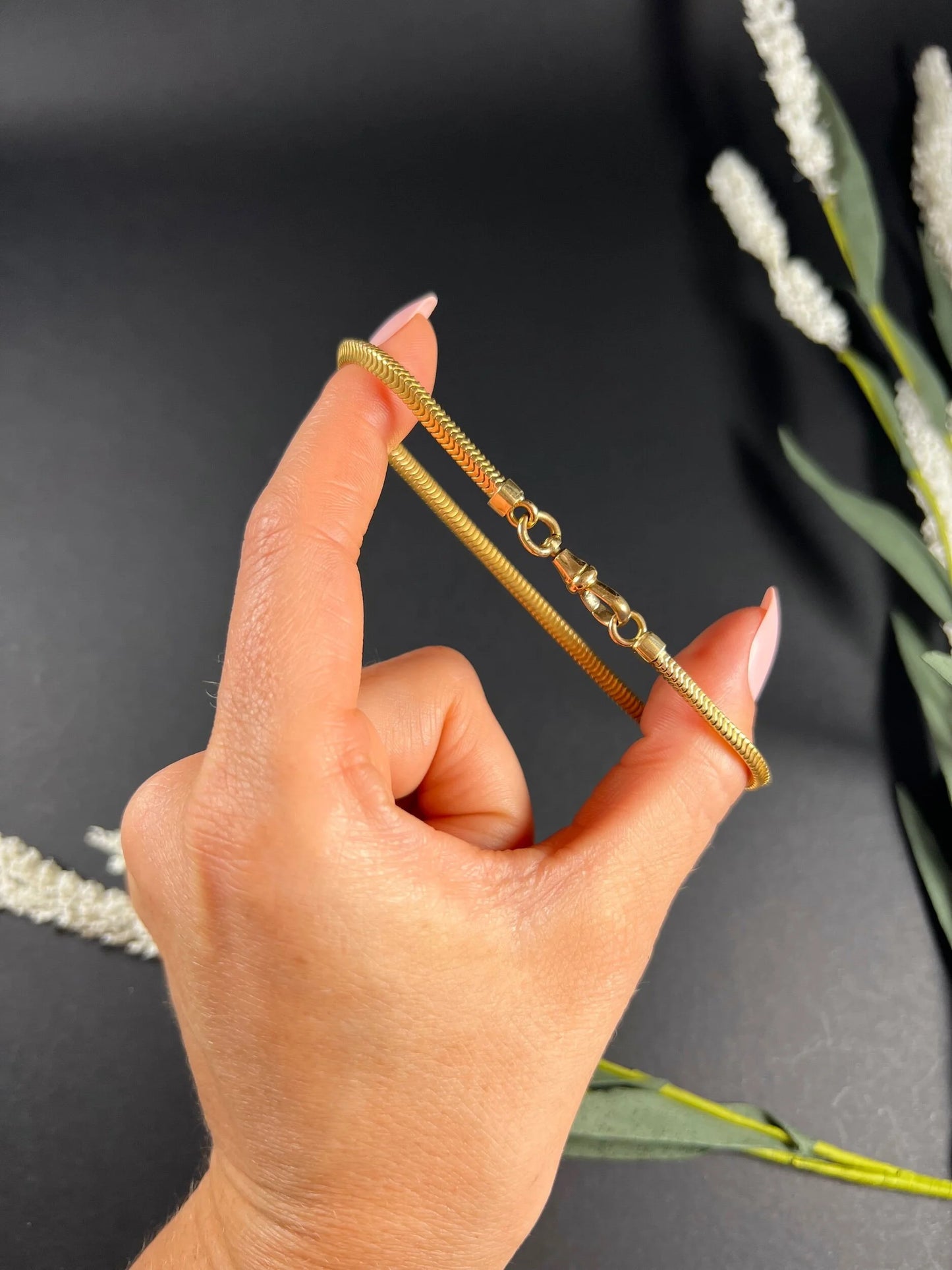 A yellow gold snake link bracelet, held in a hand