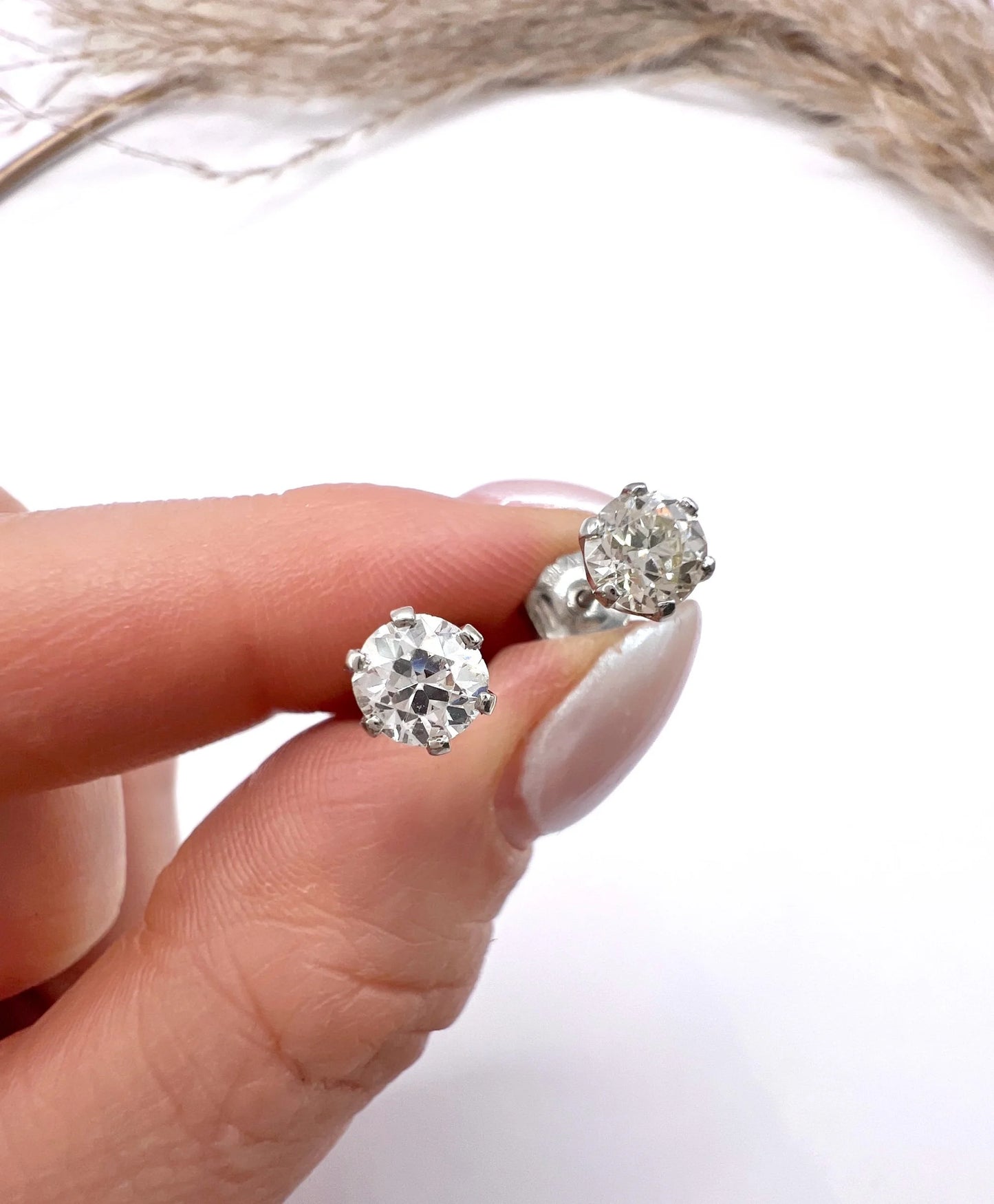 A pair of single stone round diamond stud earrings claw set in platinum, held in a hand