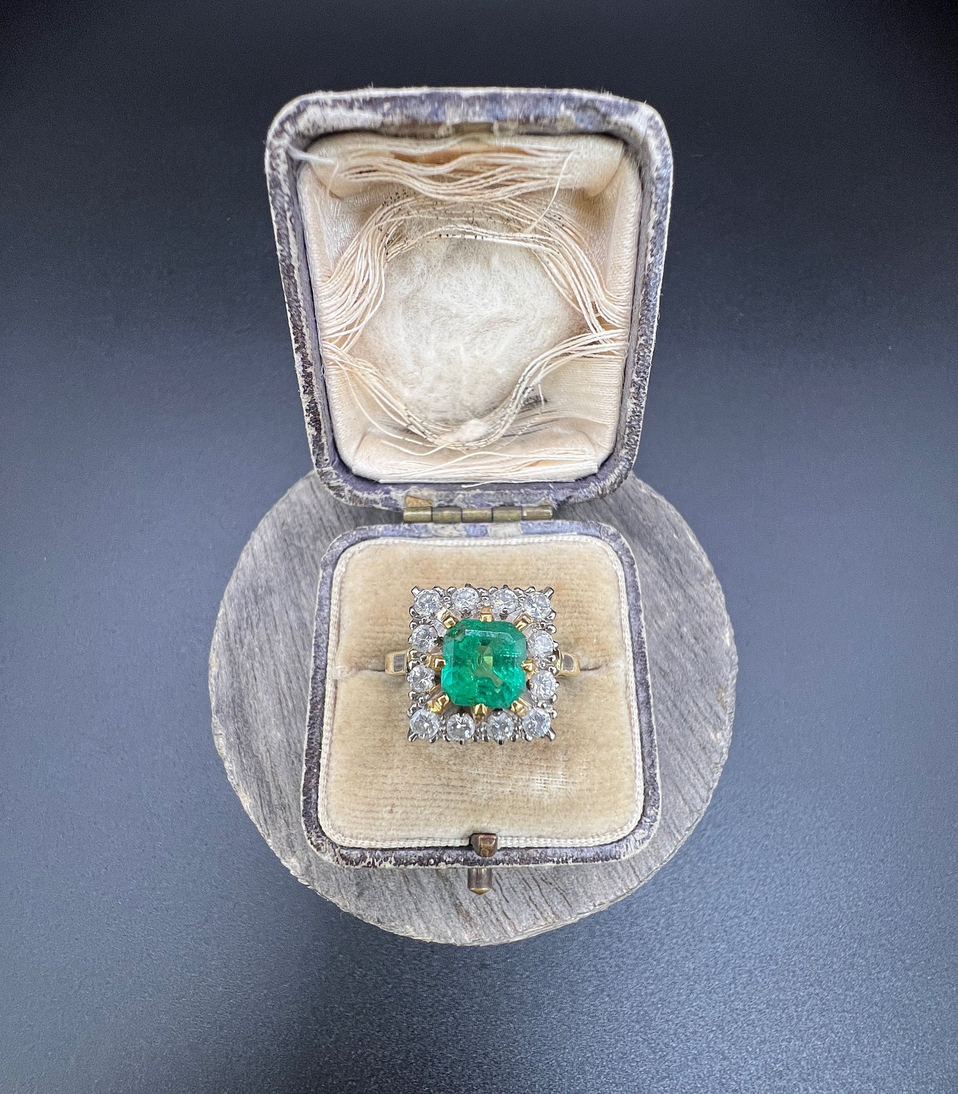 A square shaped emerald and diamond cluster ring in yellow and white gold, in a ring box