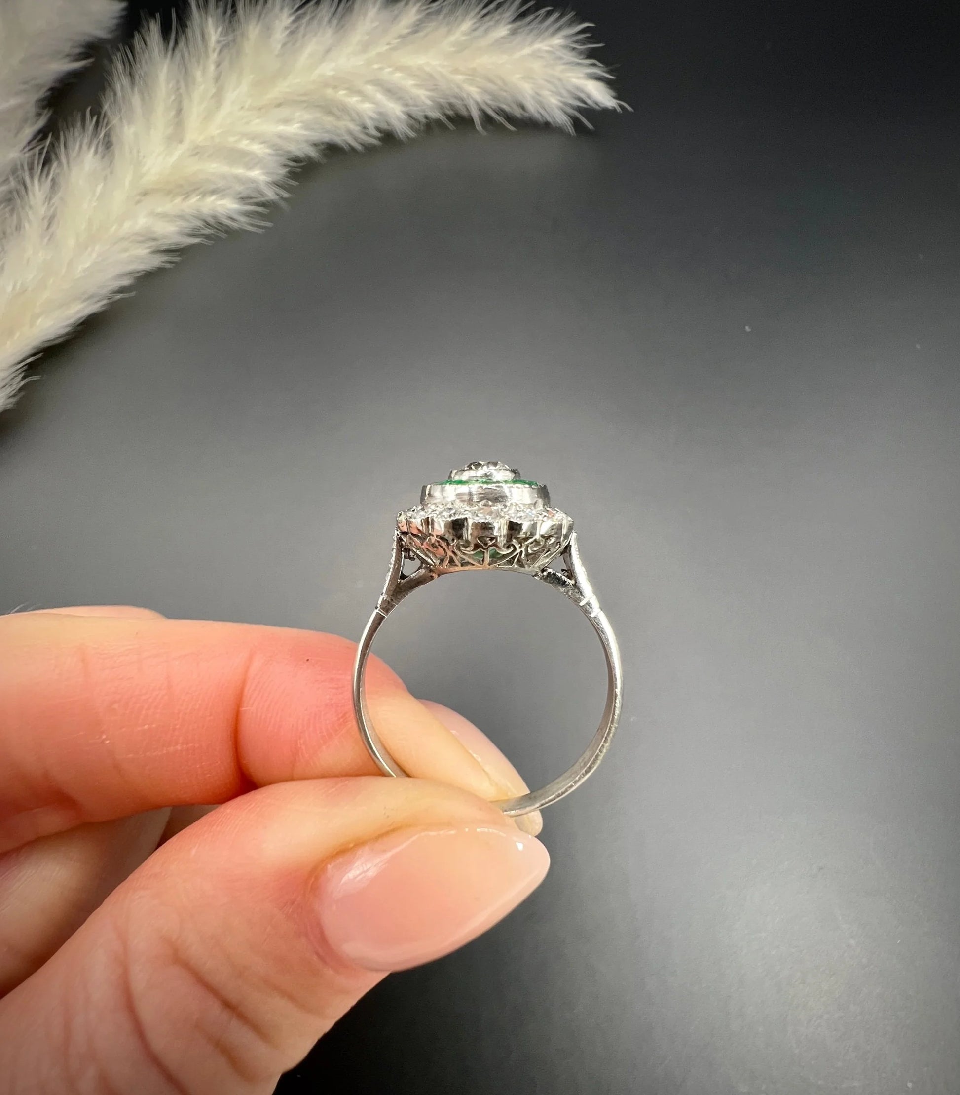An emerald and diamond target cluster ring in platinum, held in a hand