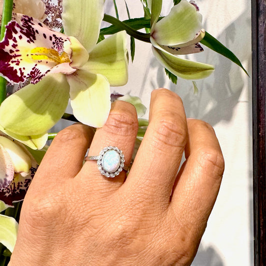 An oval opal and diamond cluster ring in platinum, modelled on a hand