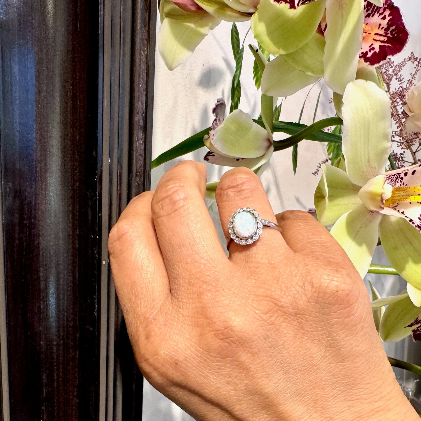 An oval opal and diamond cluster ring in platinum, modelled on a hand