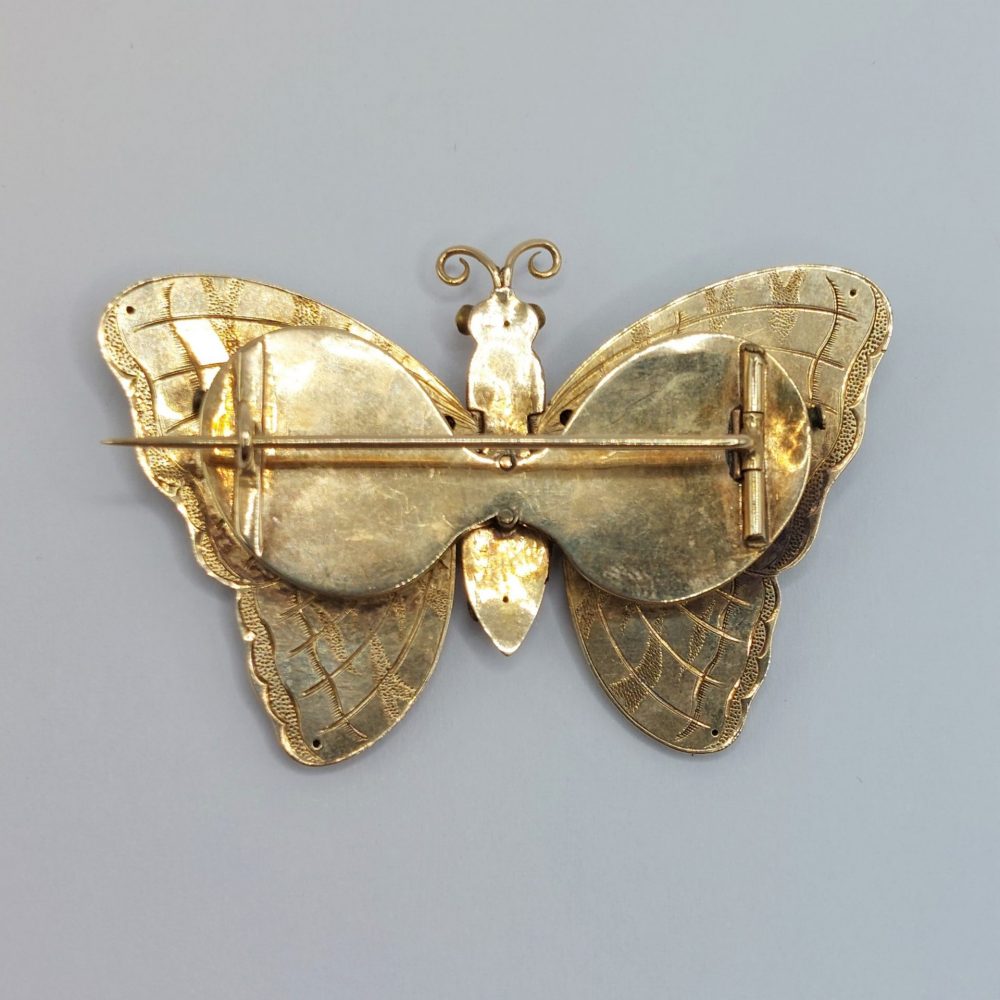 Rare Antique Gold Articulated Butterfly Locket Brooch; green gold butterfly decorated with black enamel tiger stripes and engraving, with cabochon rubies, emeralds and pearls to the wing tips which open to reveal two locket compartments beneath