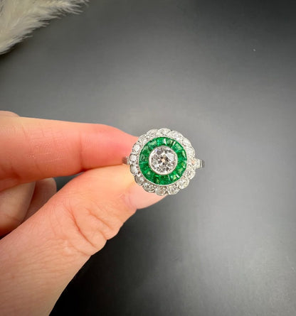 An emerald and diamond target cluster ring in platinum, held in a hand