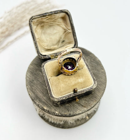 A cushion shaped amethyst cluster ring with a pearl border, in yellow gold, in a ring box