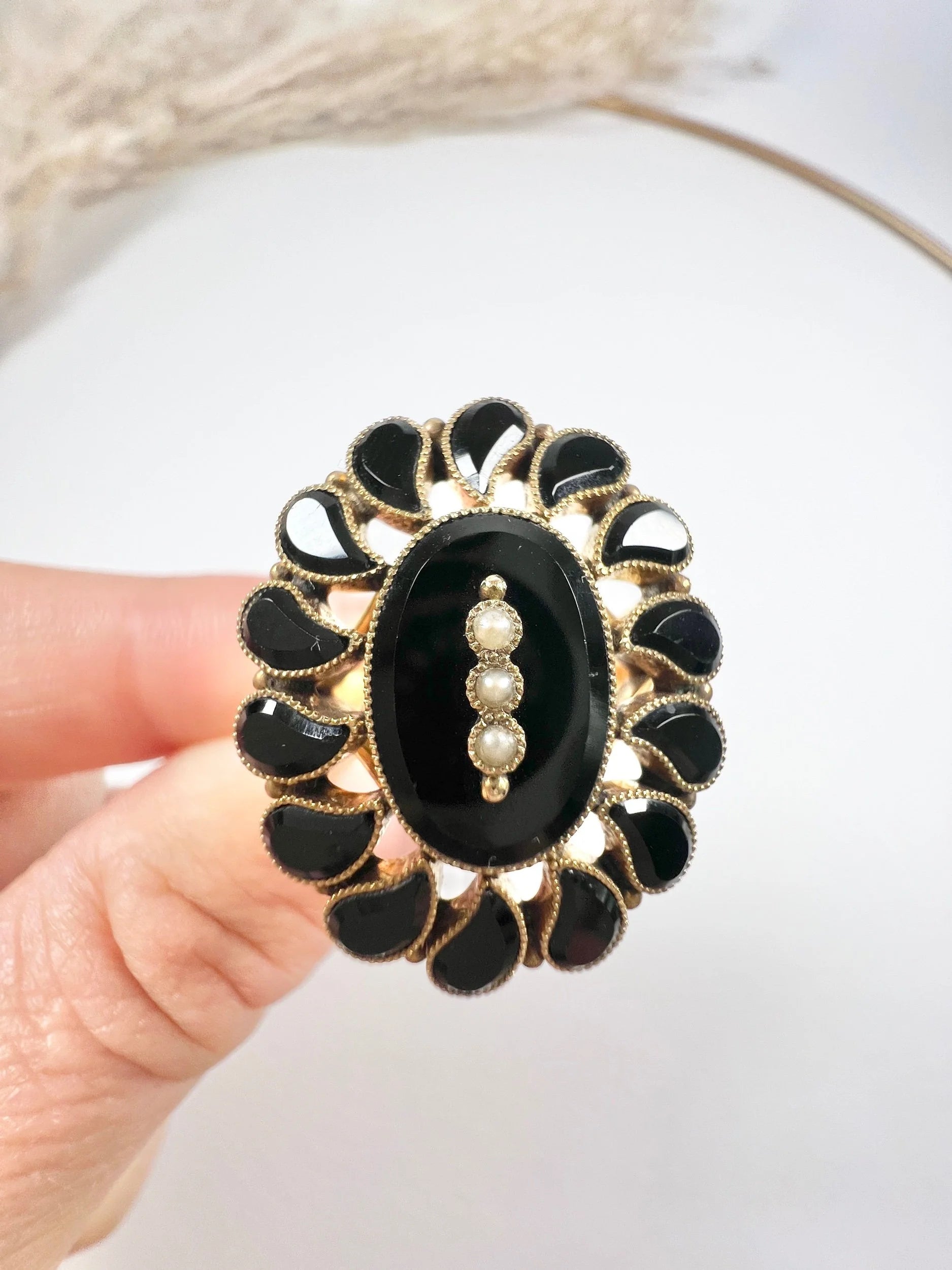 A black onyx and seed pearl fancy halo cluster ring in yellow gold, held in a hand