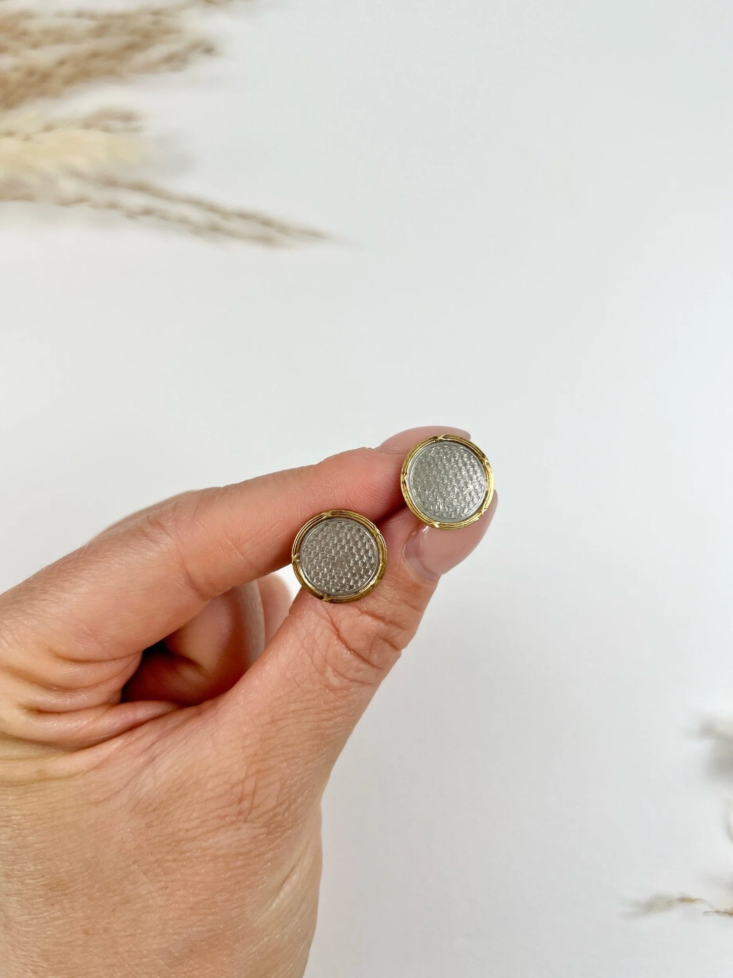 A pair of circular platinum and yellow gold cufflinks, held in a hand