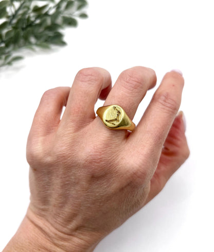 A yellow gold oval signet ring with a seal engraved heraldic crest, modelled on a hand